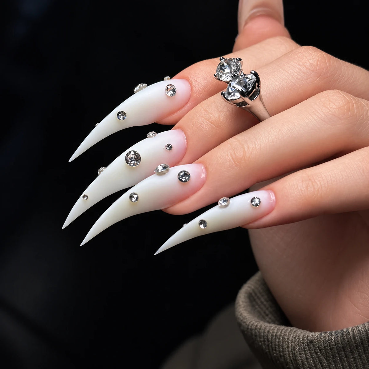Close-up of matte white pointed claw press-on nails featuring clear rhinestone embellishments and an extra-long shape.