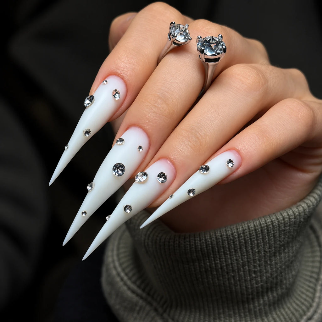 Extra-long matte white claw press-on nails with sparkling rhinestone accents, displayed on a hand against a dark background.