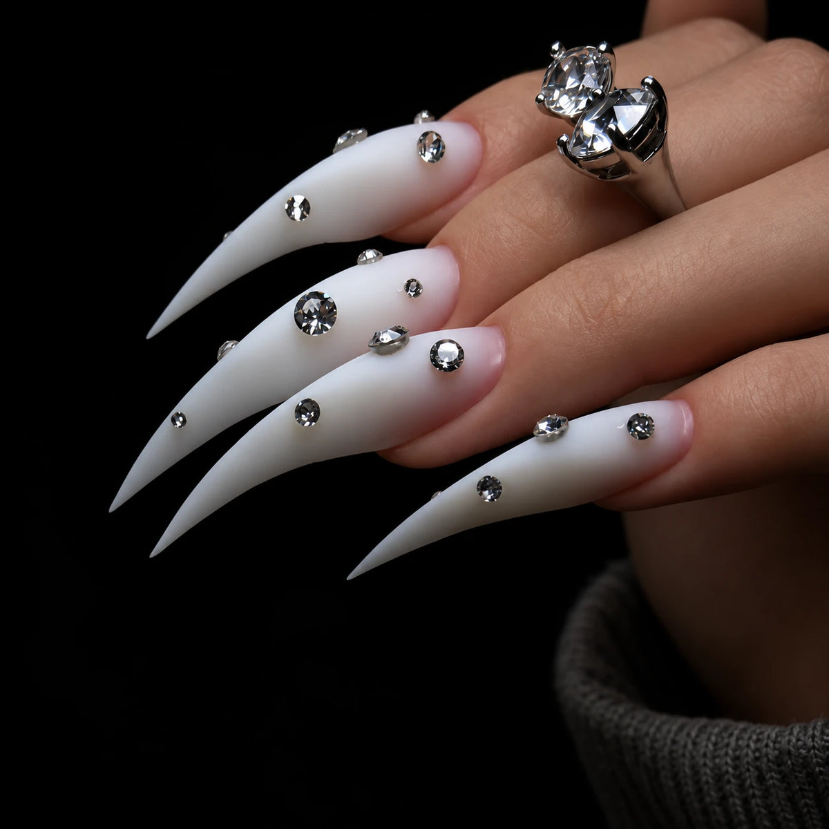 Matte white Dragon Claw press-on nails with extra-long pointed tips and clear rhinestone accents, shown on one hand.