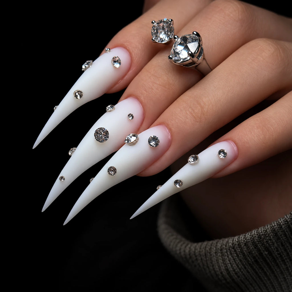 Detailed angled view of matte white Dragon Claw press-on nails with extra-long tapered tips and clear rhinestone accents.