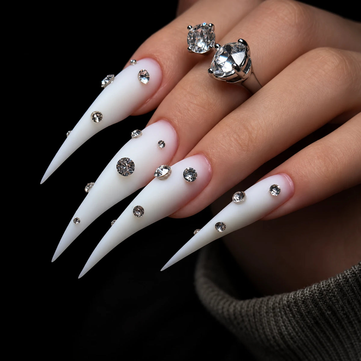 Detailed angled view of matte white Dragon Claw press-on nails with extra-long tapered tips and clear rhinestone accents.